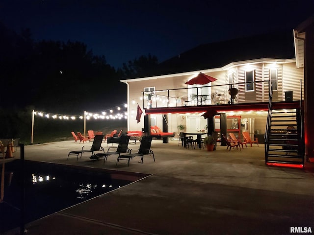 back house at twilight featuring a balcony and a patio