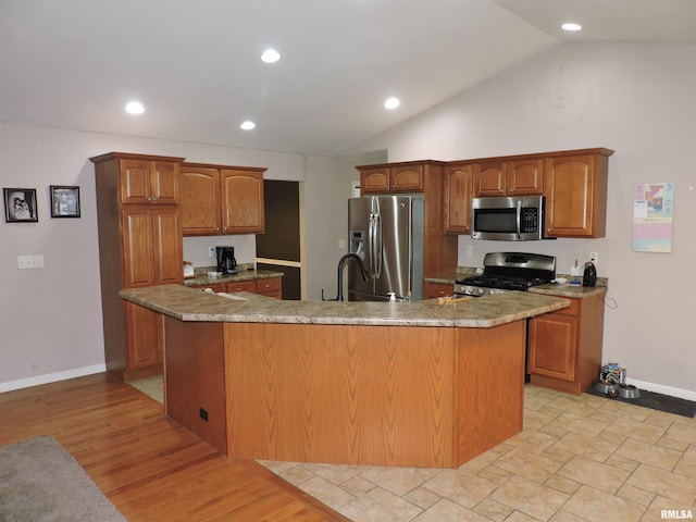 kitchen with stainless steel appliances, sink, light hardwood / wood-style flooring, lofted ceiling, and an island with sink