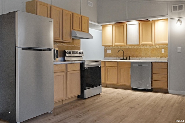 kitchen with sink, light brown cabinets, tasteful backsplash, appliances with stainless steel finishes, and light wood-type flooring