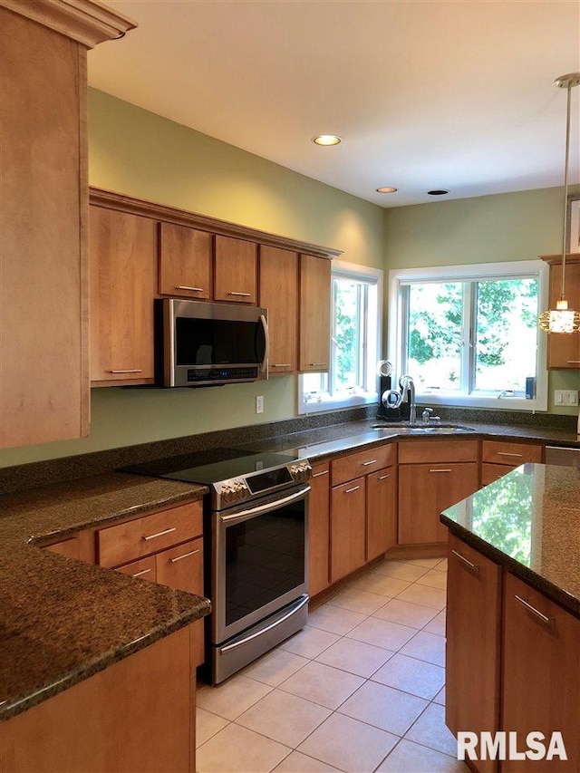 kitchen with sink, stainless steel appliances, dark stone countertops, decorative light fixtures, and light tile patterned floors