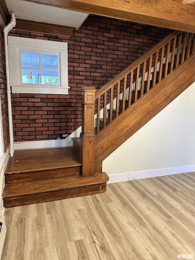 staircase featuring wood-type flooring and brick wall