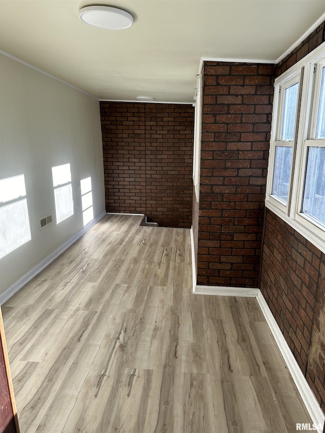 empty room featuring light hardwood / wood-style flooring, ornamental molding, and brick wall