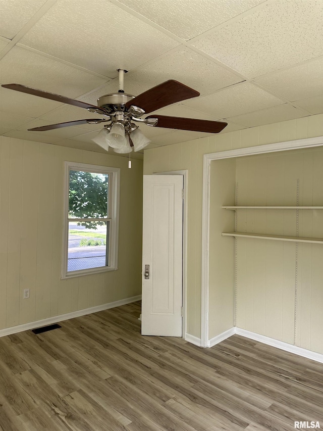 unfurnished bedroom featuring a paneled ceiling, ceiling fan, a closet, and hardwood / wood-style flooring