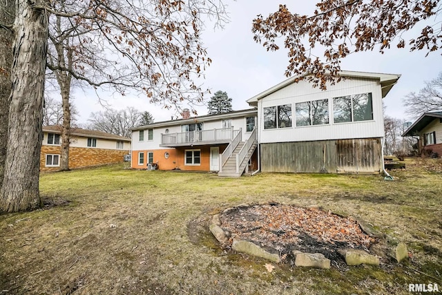 rear view of house with a fire pit, a deck, and a lawn