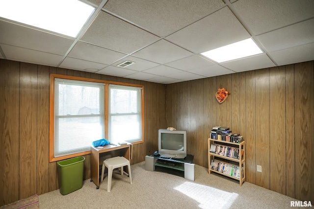 interior space featuring carpet flooring, a drop ceiling, and wooden walls