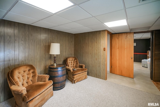 sitting room with a drop ceiling, light colored carpet, and wooden walls