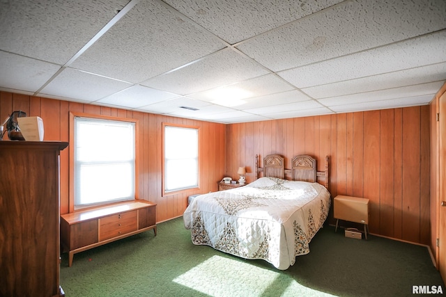 unfurnished bedroom featuring carpet flooring, a drop ceiling, and wooden walls