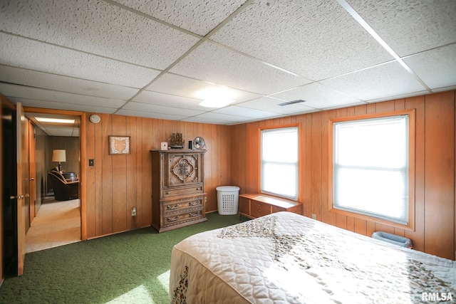 carpeted bedroom with a drop ceiling and wood walls