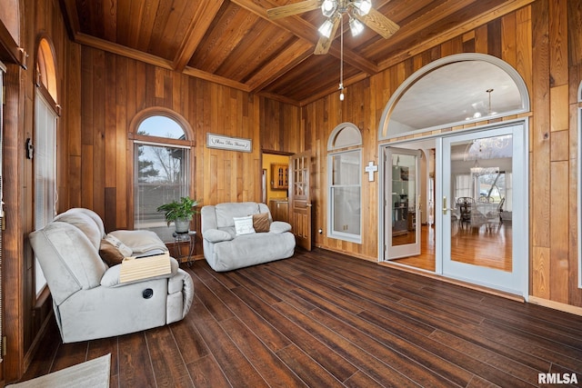 sitting room with ceiling fan with notable chandelier, beam ceiling, wood ceiling, and wooden walls