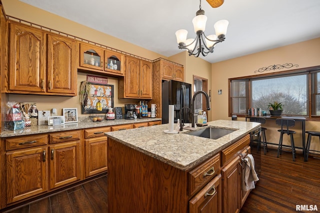 kitchen featuring a kitchen island with sink, an inviting chandelier, black refrigerator, hanging light fixtures, and sink