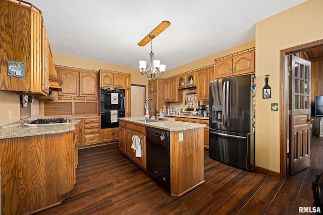 kitchen featuring light stone counters, a kitchen island with sink, sink, black appliances, and an inviting chandelier