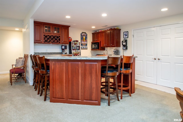 kitchen featuring a breakfast bar area, kitchen peninsula, black microwave, and light colored carpet