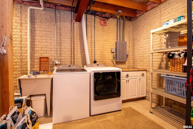 laundry room with washing machine and clothes dryer, electric panel, cabinets, and brick wall