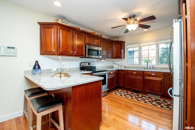 kitchen with light stone counters, kitchen peninsula, a kitchen bar, appliances with stainless steel finishes, and light wood-type flooring