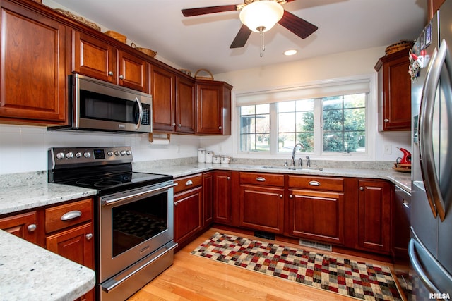 kitchen with light stone countertops, appliances with stainless steel finishes, ceiling fan, sink, and light hardwood / wood-style floors