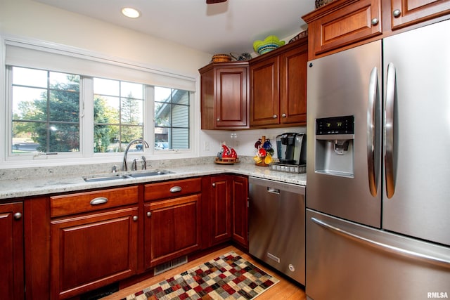 kitchen with appliances with stainless steel finishes, light hardwood / wood-style flooring, light stone counters, and sink