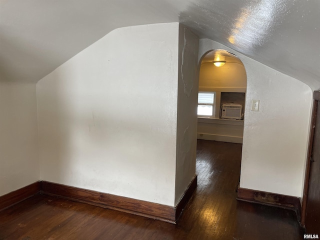 additional living space featuring dark hardwood / wood-style flooring, vaulted ceiling, and an AC wall unit