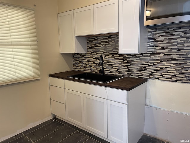 kitchen with dark tile patterned floors, backsplash, sink, and white cabinets