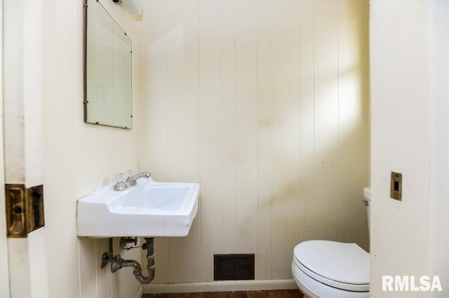 bathroom featuring toilet, wooden walls, and sink