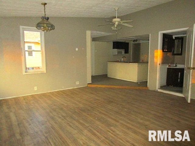 unfurnished living room featuring a textured ceiling, ceiling fan with notable chandelier, lofted ceiling, and dark wood-type flooring