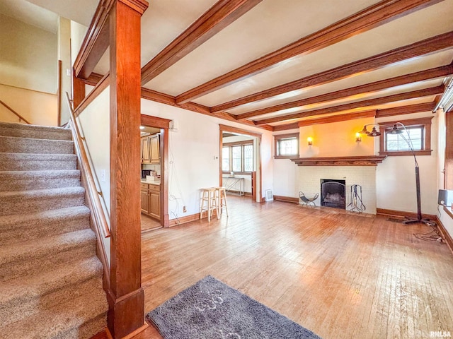 living room featuring beamed ceiling, light wood-type flooring, and a fireplace