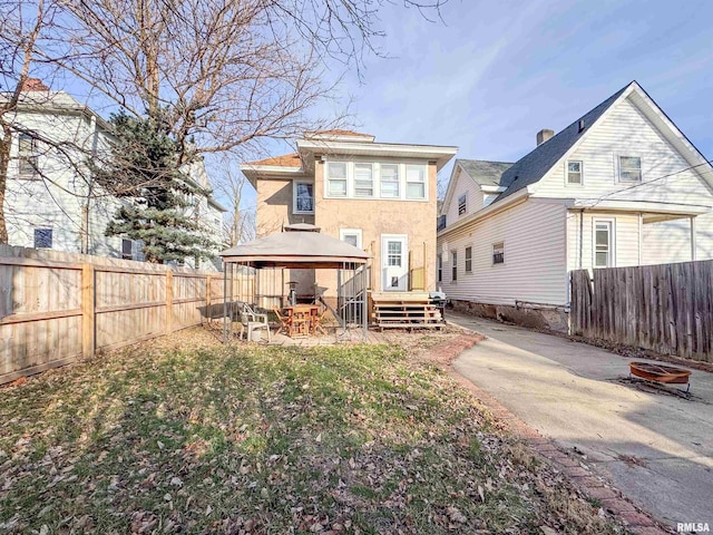 rear view of property with a gazebo, a deck, an outdoor fire pit, and a patio