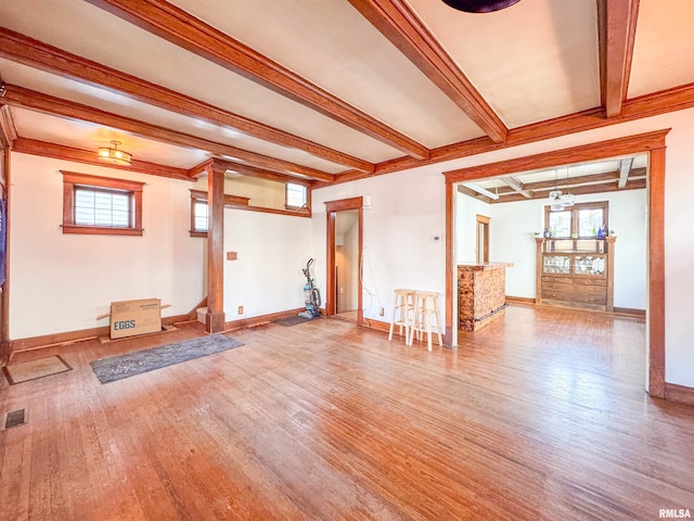 unfurnished living room featuring beamed ceiling, wood-type flooring, and a wealth of natural light