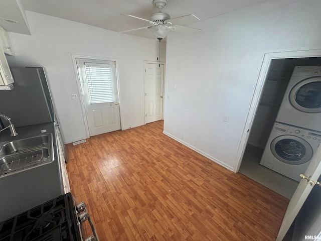 kitchen featuring stacked washer and clothes dryer, white cabinets, sink, ceiling fan, and light hardwood / wood-style floors