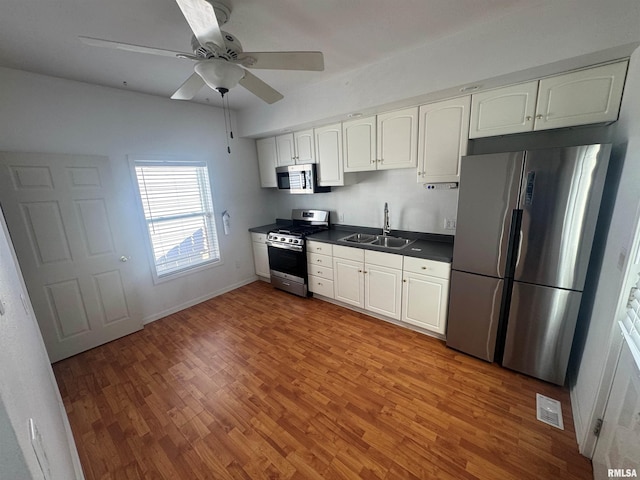 kitchen featuring stainless steel appliances, ceiling fan, sink, wood-type flooring, and white cabinetry