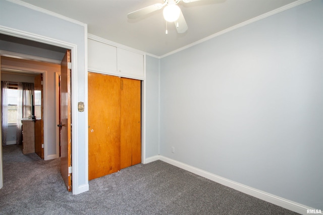 unfurnished bedroom with dark colored carpet, a closet, ceiling fan, and crown molding