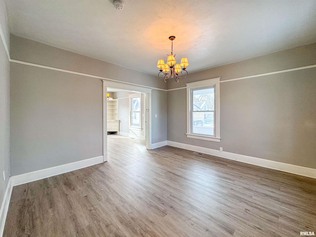 empty room with hardwood / wood-style floors and a notable chandelier