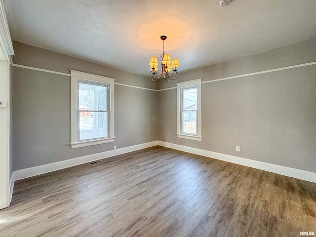 spare room featuring hardwood / wood-style flooring, a healthy amount of sunlight, and a notable chandelier