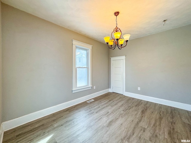 empty room with a notable chandelier and wood-type flooring