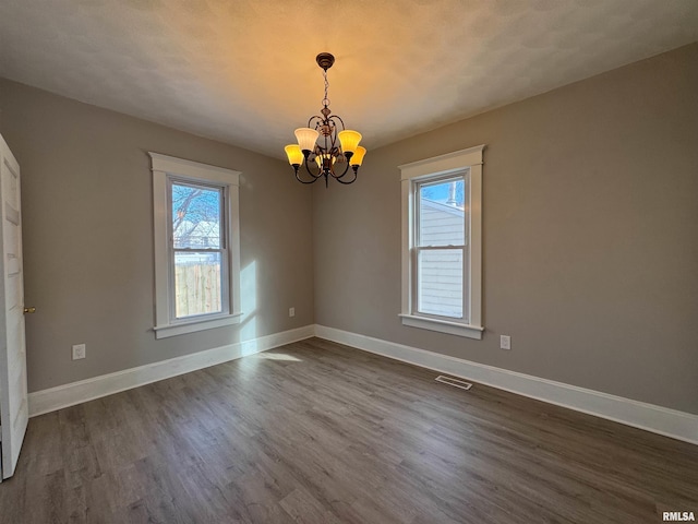 empty room with dark hardwood / wood-style flooring, a textured ceiling, and an inviting chandelier