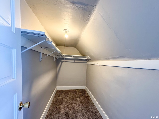 spacious closet featuring vaulted ceiling and dark colored carpet