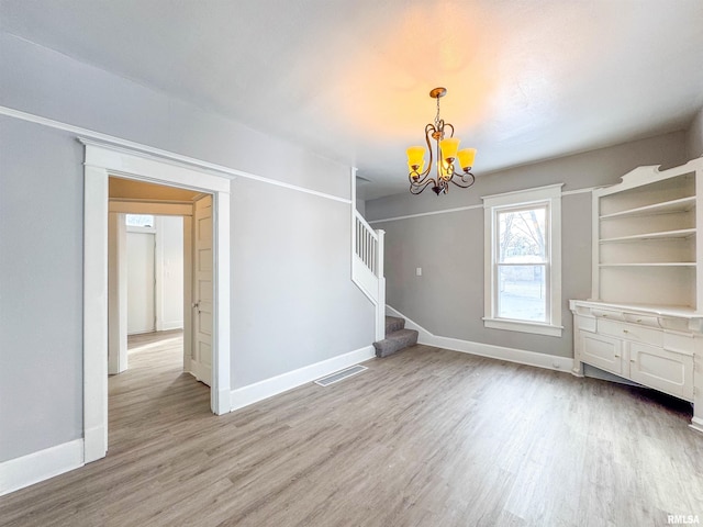 spare room featuring light wood-type flooring and a chandelier