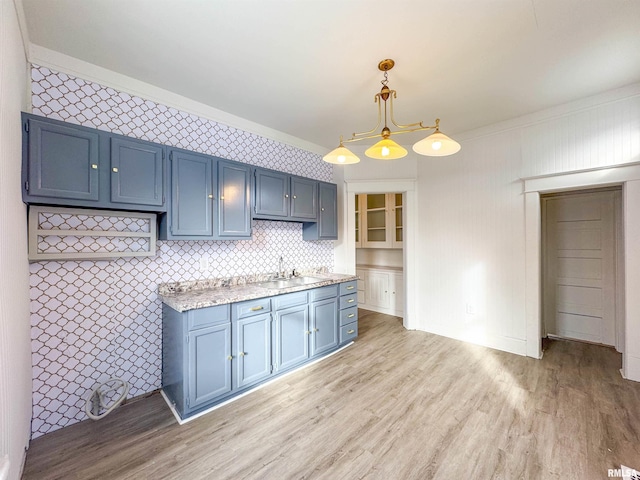 kitchen with sink, light hardwood / wood-style flooring, blue cabinets, pendant lighting, and ornamental molding