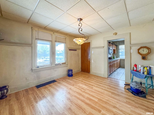 unfurnished dining area featuring light hardwood / wood-style flooring and a drop ceiling