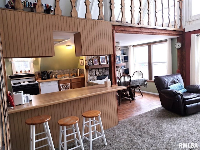 kitchen featuring a stone fireplace, light colored carpet, white appliances, and a breakfast bar area