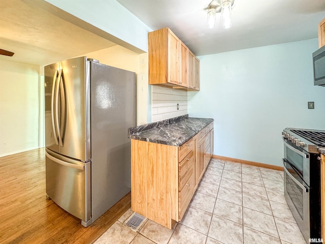 kitchen with dark stone countertops, decorative backsplash, light brown cabinetry, light tile patterned floors, and appliances with stainless steel finishes