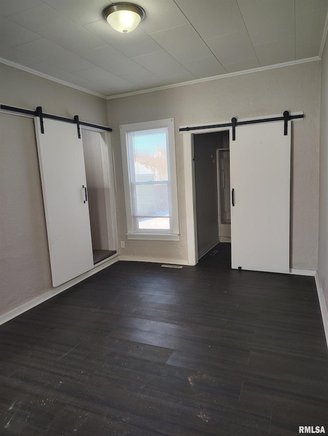 spare room featuring dark hardwood / wood-style flooring, a barn door, and crown molding