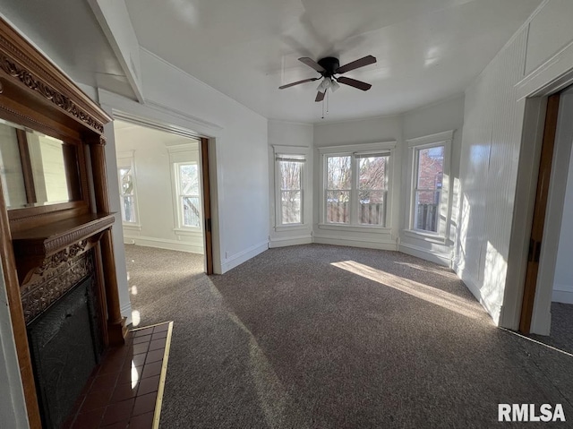 unfurnished living room with ceiling fan, dark carpet, and a tiled fireplace