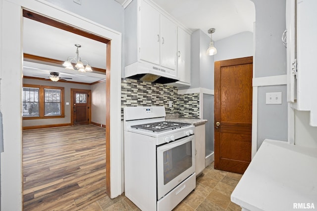 kitchen featuring range hood, backsplash, decorative light fixtures, ceiling fan with notable chandelier, and white gas range oven