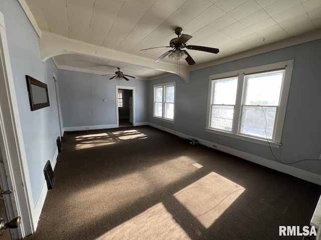 empty room featuring a wealth of natural light, dark colored carpet, beamed ceiling, and ceiling fan