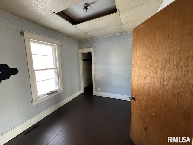 spare room with a drop ceiling and dark hardwood / wood-style floors