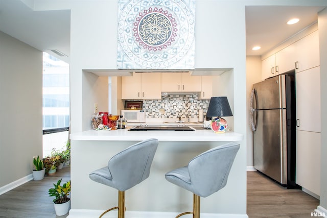 kitchen featuring kitchen peninsula, backsplash, light hardwood / wood-style flooring, and stainless steel refrigerator