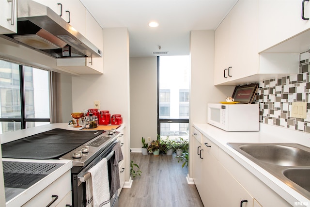 kitchen with stainless steel range with electric stovetop, white cabinets, sink, light wood-type flooring, and tasteful backsplash