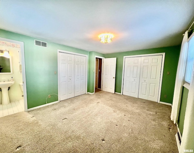 unfurnished bedroom featuring two closets, connected bathroom, carpet floors, and sink