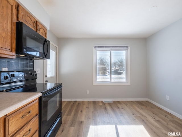 kitchen with decorative backsplash, black appliances, and light hardwood / wood-style floors