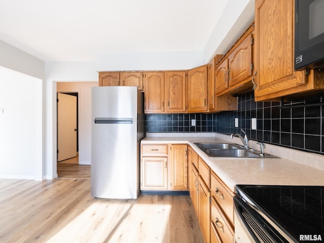 kitchen featuring stainless steel fridge, light wood-type flooring, sink, and tasteful backsplash